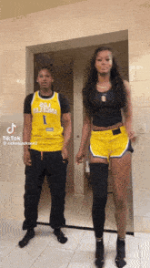 a man in a yellow jersey with the number 1 on it stands next to a woman in shorts