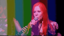 a woman with red hair is singing into a microphone in front of a colorful background