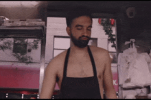 a shirtless man in an apron stands in front of a pink sign that says k