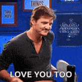 a man is sitting in front of a microphone with the words `` love you too '' written on it .