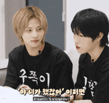 two young men are sitting next to each other and one of them is wearing a black shirt with chinese writing