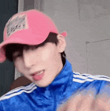 a young man wearing a pink baseball cap and a blue jacket is making a funny face .