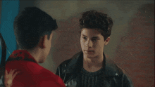 a man in a red jacket talks to another man in a black leather jacket