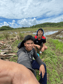 a young man wearing a yonex shirt sits next to another young man in a field