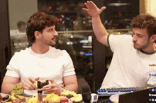 two men are sitting at a table with a laptop that says freez