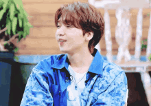 a young man wearing a blue tie dye shirt is smiling while sitting in a chair .