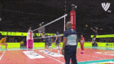 a volleyball game is being played on a court with a referee standing in front of the net .