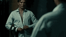 a man in a white shirt is standing in front of a mirror and adjusting his shirt .