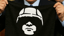 a man in a suit and tie holds a black cloth with a white face on it