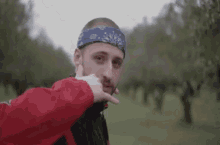 a man wearing a bandana and a red jacket is making a hand gesture in a field .