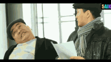a man in a hat and scarf holds a piece of paper in front of another man in a hat and scarf ..