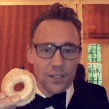 a man in a tuxedo and bow tie is holding a donut .