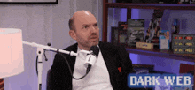 a man in a suit is sitting in front of a microphone with a dark web logo in the background .