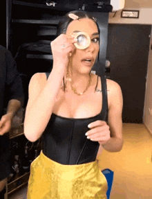 a woman wearing a black top and yellow skirt is holding a magnifying glass over her eye