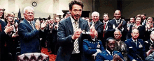 a man in a suit and tie is standing in front of a crowd of people who are clapping .