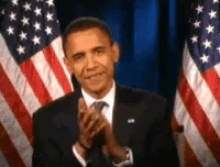 a man in a suit and tie is applauding in front of american flags