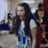 a girl wearing overalls and a backpack is standing in a hallway with her mouth wide open
