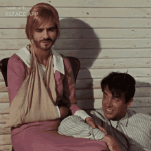 a man with a bandage on his arm is sitting next to another man who is wearing a pink dress