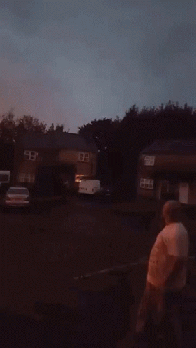 A man holding a large stick outside during a thunderstorm. As the lightning strikes he lifts the stick in the sky looking like a wizard with a magical staff getting struck by lightning.