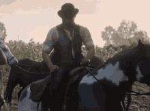 a man in a hat is riding a black and white horse in a field .