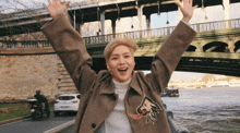 a woman with her arms in the air stands in front of a bridge