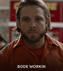 a man with a beard wearing an orange shirt and the name bode workin on the bottom