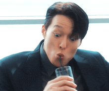 a man in a suit is drinking from a glass with a straw in his mouth