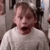 a young boy is making a surprised face while wearing a white sweater .