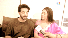 a man and woman are sitting on a couch being interviewed by a reporter