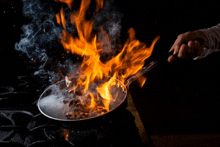 a person is cooking food in a frying pan on a stove with flames coming out of it