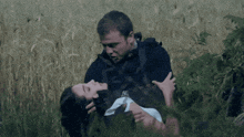a man is holding a woman in his arms in a field of tall grass