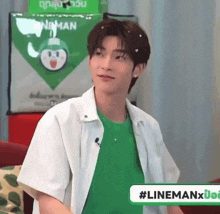 a young man wearing a green shirt and a white jacket is sitting in front of a sign that says lineman .
