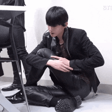 a man in a black suit sits on the floor in front of a sign that says ' & te '