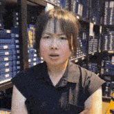 a woman in a black shirt is standing in front of a shelf with blue boxes .