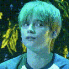 a young boy with green hair is wearing a blue shirt and looking at the camera .