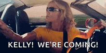 a woman is driving a car with the words `` kelly ! we 're coming ! '' on the screen .