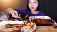 a woman in a blue shirt is eating a plate of food with a fork
