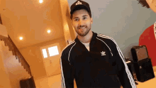 a man wearing a black adidas jacket and hat