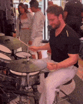 a man in a black shirt is playing drums in front of a group of people