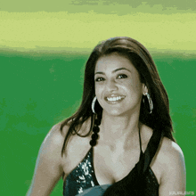 a woman wearing a black top and hoop earrings is smiling on a green background .