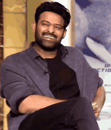 a man with a beard is smiling while sitting down with his legs crossed .