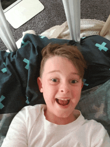 a young boy laying on a bed with a blanket that has a cross on it