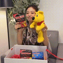 a woman is holding a stuffed teddy bear and a bag of haribo