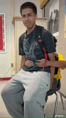 a man wearing a gray shirt with the word jordan on it sits on a chair
