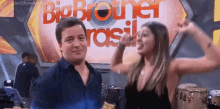 a man and a woman are posing in front of a big brother brasil sign