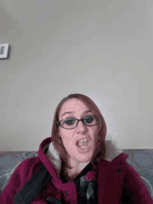 a woman wearing glasses and a pink coat making a face