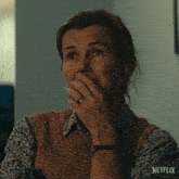 a woman is covering her mouth with her hand and a netflix logo is visible in the corner