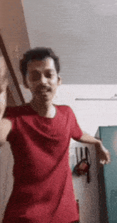 a man in a red t-shirt is dancing in a room with his hands in the air .