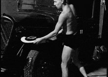 a black and white photo of a man in underwear holding a frisbee with the letter l on it
