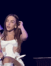 a woman in a white dress is sitting on a stage with her eyes closed and holding her hair .